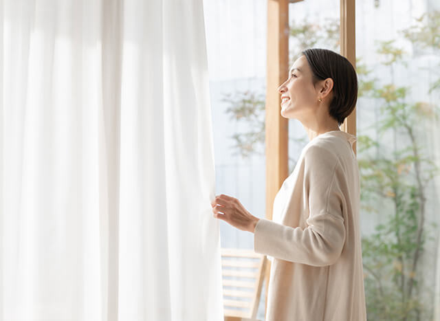 カーテン越しに庭を見る女性